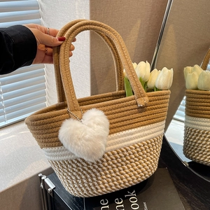 Handgewebte Strohtasche mit braun-weißem Muster und einem flauschigen Herzanhänger