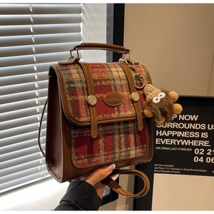 Detail eines Tweed-Karo-Rucksacks mit Lederschnallen und süßem Monster-Plüsch-Anhänger