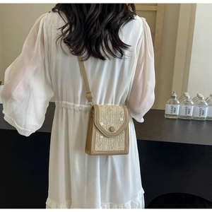 Détail d'un sac bandoulière en paille avec broderie florale blanche et lanière en cuir