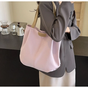 Detail of a large pink canvas tote bag with khaki straps worn by a model in a cozy cafe