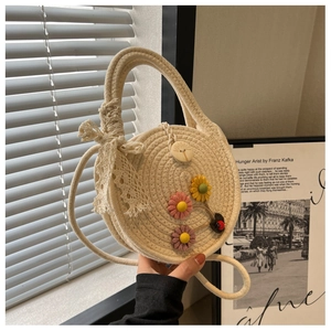 Detail der runden cremefarbenen Strohtasche mit bunten Blumen und Spitzenschleife