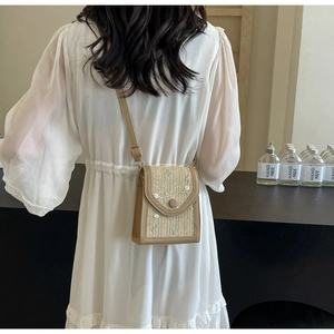 Détail d'un sac bandoulière tissé beige avec broderie florale sur le rabat et fine lanière