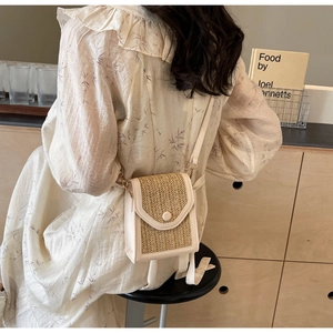 Detail of a cream woven crossbody bag with round buckle on a textured flap cover