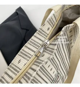 Detail of the smooth silver metal zipper and brand label on a striped corduroy tote bag