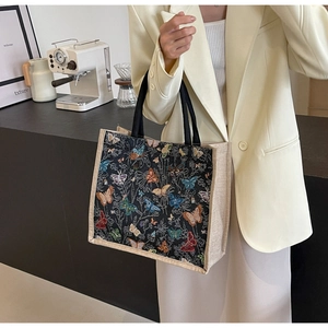 Détail de la broderie papillon et des coutures en toile sur un sac cabas noir porté