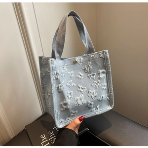 Close-up of light blue canvas tote bag with 3D floral texture and gold magnetic clasp