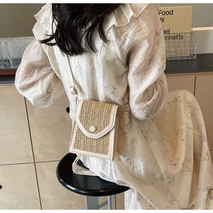 Detail of hand-woven straw crossbody phone bag with leather trim and round buckle