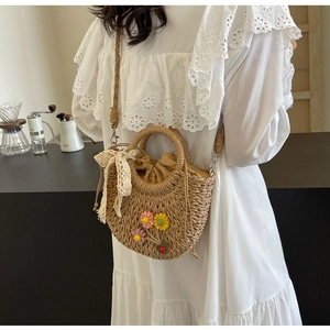 Detail of hand-woven straw crossbody bag with floral accents and lace bow on a model