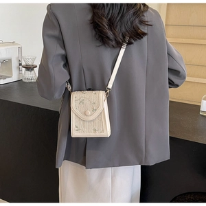 Détail du sac à téléphone en paille brodée porté en bandoulière dans un café
