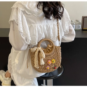 Detail of straw bag featuring embroidered flowers, lace bow, and drawstring closure