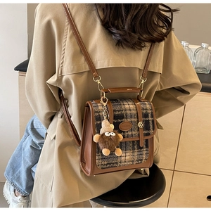 Detailansicht eines Vintage-Rucksacks mit Karomuster, braunem PU-Leder und Bären-Anhänger