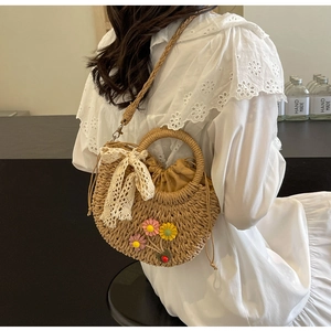 Detail of straw woven crossbody bag featuring floral accents and lace ribbon details