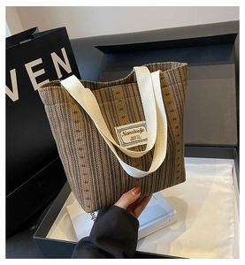 Close-up of brown striped canvas tote bag with white woven handles and text patch detail