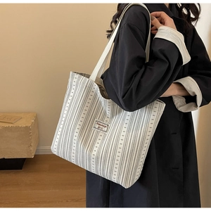 Detail of cream corduroy tote bag with grey stripes and logo patch worn by model