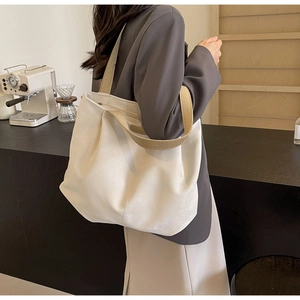 Close-up of stylish off-white tote bag with khaki straps shown on a model in a cafe