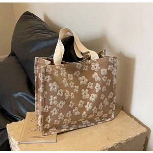 Detail view of brown canvas tote bag with floral pattern on a stone pedestal