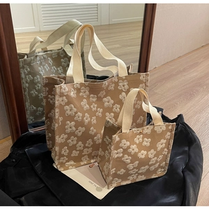 Detail view of large and small canvas tote bags with white floral prints and woven handles