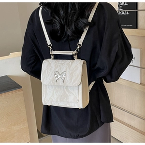 Détail du sac à dos crème avec texture plissée et boucle papillon argentée sur tenue noire