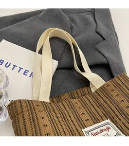 Detail of brown corduroy tote bag with woven texture and reinforced cream webbing handles