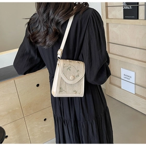 Détail d'un sac bandoulière en paille beige avec broderie florale porté par un mannequin