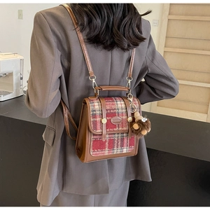 Detail eines Vintage-Rucksacks mit Karomuster, Lederbesatz und Plüsch-Anhänger im Café