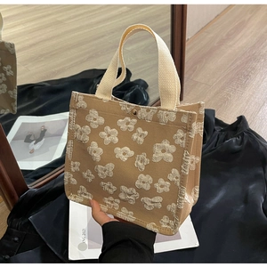 Detailed view of canvas tote featuring textured floral embroidery and braided handles