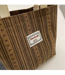 Detail of brown striped corduroy tote bag showing woven brand label and fabric texture
