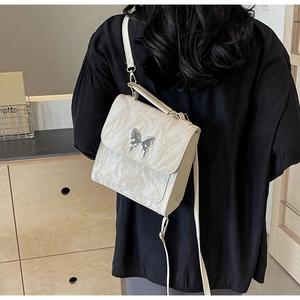 Détail du sac à dos crème en cuir verni plissé avec boucle papillon argentée élégante