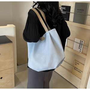 Detail of light blue tote bag with wide brown leather strap and fashion label detail