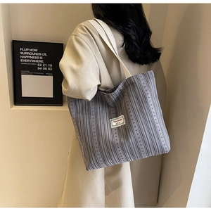 Detail showing grey corduroy tote bag texture and white strap in minimalist setting