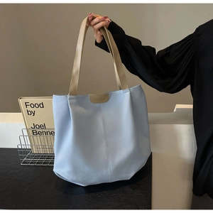 Detail view of light blue tote bag with tan straps and metal fashion emblem on front