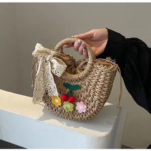 Detailed shot of handmade straw bag featuring crochet cherries and white lace ribbon
