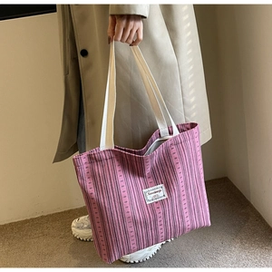 Detail of pink corduroy tote bag featuring a white logo patch and cream woven handles