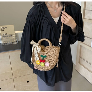 Straw basket bag with cherry and flower charms, showing crossbody carry style on model