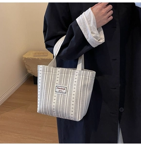 Detail view of a striped canvas handbag with woven brand label and sturdy handles