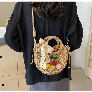 Detail view of woven straw shoulder bag with lace bow and colorful crochet cherry patches