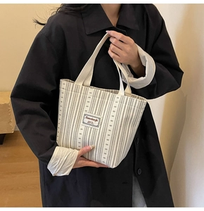 Close-up of beige striped canvas tote bag with woven label held by a model in black coat