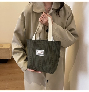 Detail of dark green striped knit handbag featuring a branded woven label and cream straps