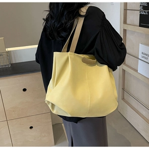 Detail of yellow leather tote bag with embossed Fashion label worn by model on shoulder