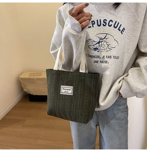 Detail of dark green corduroy tote bag with woven handles and minimalist fabric label