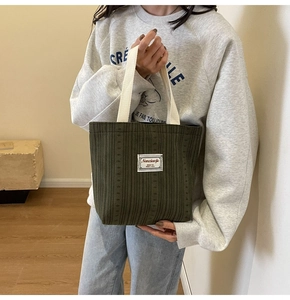 Detail of dark green corduroy tote bag with white canvas handles and brand patch