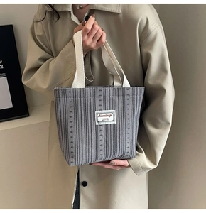 Detail of grey vertical striped tote bag with white woven handles and text patch