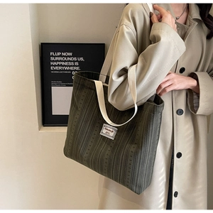 Detail of dark green corduroy tote bag featuring wide cream strap and woven logo label