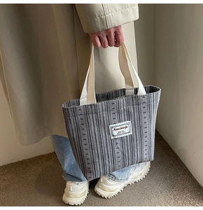 Close-up of striped canvas tote bag with white handles held by a model in a trench coat