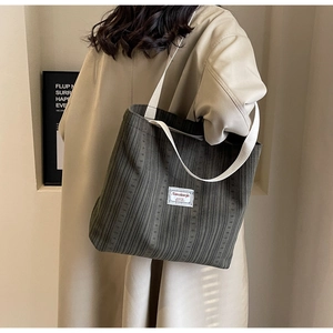 Detail of olive green corduroy tote bag with woven straps worn on shoulder by model