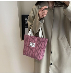 Detailed view of pink corduroy handbag featuring white canvas straps and logo on a beige coat
