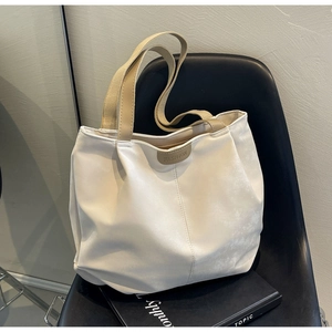Detail of minimalist cream tote bag with fashion patch resting on a modern black chair