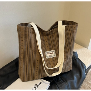 Detail of brown corduroy tote bag with woven label and cream canvas shoulder strap