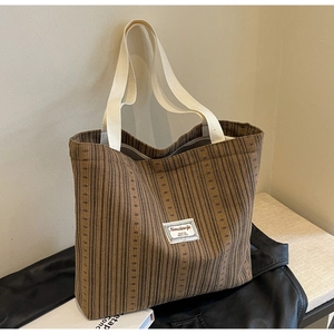 Detail of striped corduroy tote bag showing reinforced handles and brand patch design