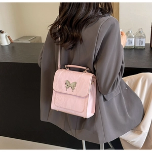 Gros plan du sac bandoulière rose clair avec boucle papillon sur un blazer gris